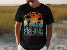 "Embrace your passion for solitude and fishing with this humor-filled graphic tee. Featuring the silhouette of a serene fisherman against a vibrant sunset backdrop and the words \"I'm Not Anti-Social, I'd Just Rather Be Fishing Than Talking To Idiots\", this shirt is perfect for those who find peace by the water. Made from comfortable materials, it's ideal for casual outings, beach trips, or a day out on the boat. A great gift for anglers, introverts, or anyone who enjoys a good laugh. Ready to wear, it's sure to be a conversation starter and a favorite wardrobe staple for any fishing enthusiast." Summer Fishing T-shirt With Crew Neck, Summer Crew Neck T-shirt For Fishing, Crew Neck T-shirt For Summer Fishing, Fisherman Silhouette, Outdoor Wardrobe, Sunset Backdrop, Angel T Shirt, Sunset Graphic, Casual Beach Wear