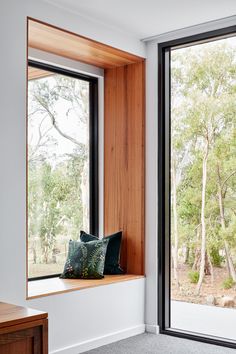 a window seat with pillows on it in front of a large window overlooking the woods