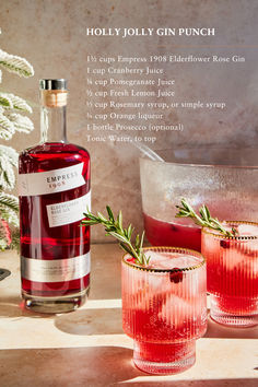 two glasses filled with red liquid and rosemary sprigs next to a bottle of holly gin punch