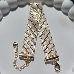 two white and gold bracelets with chains on top of each beaded stranding