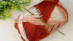 a ball of yarn and knitting needles on a white surface next to some flowers with green leaves