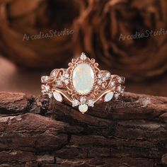 a white opal and diamond ring sitting on top of a piece of drift wood