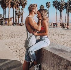 a man and woman are sitting on a wall at the beach with palm trees in the background