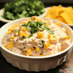 a white bowl filled with corn and salsa next to some tortilla chips on a table