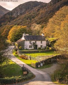 a house in the middle of a country road surrounded by trees and hills with mountains in the background