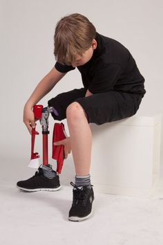 a young boy sitting on top of a red fire hydrant with his legs crossed