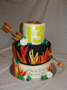 a three tiered cake decorated with flowers and an arrow is on a white tablecloth