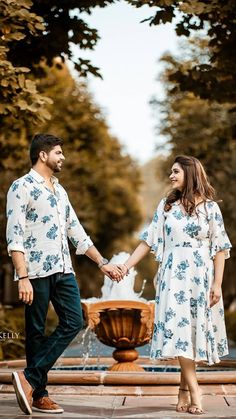 a man and woman holding hands in front of a fountain