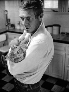 a man holding a cat in his arms and looking at the camera while standing in a kitchen