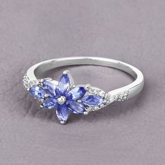 a white gold ring with blue flowers and diamonds on the side, sitting on a gray surface