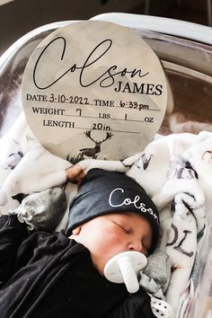 a newborn baby wrapped in a blanket and wearing a black hat with the birth date on it