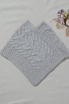 two gray knitted placemats sitting on top of a white blanket next to flowers