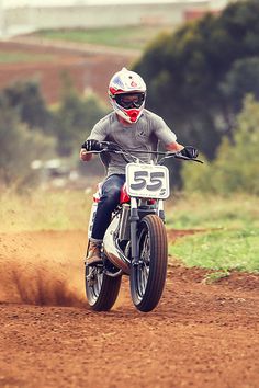 a man riding on the back of a dirt bike down a dirt road with trees in the background