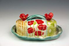 a cake with red flowers on it is sitting on a platter and sits on a white surface