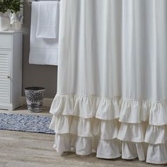 a white shower curtain with ruffles on it in a bathroom next to a rug