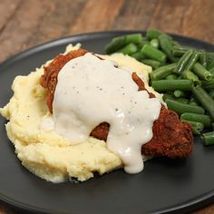 a black plate topped with mashed potatoes and green beans