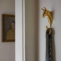 a gold horse head mounted on the wall next to a black tie holder with a man's portrait in the background