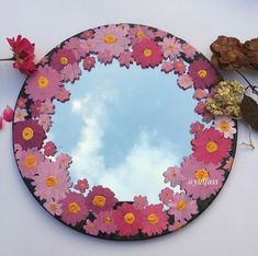 there is a mirror with pink flowers on it and some leaves around it, as well as the sky in the background