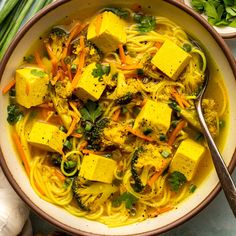 a bowl filled with tofu, noodles and broccoli on top of a table