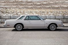 a silver car parked in front of a stone wall