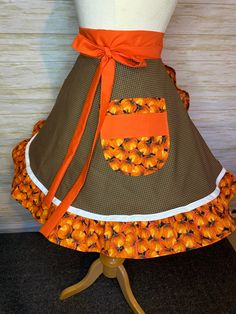 an orange and brown apron on a mannequin with ribbon around the waist that has pumpkins all over it