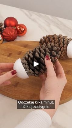 a person holding a pine cone on top of a wooden board next to christmas ornaments