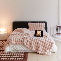 a bed covered in pink fluffy blankets next to a table with a lamp on it