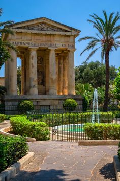 an old building with columns and pillars in the middle of a garden area next to a fountain