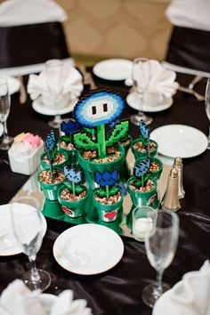 a table topped with lots of plates and cups filled with plants next to wine glasses