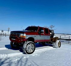 a red and silver truck parked on top of snow covered ground next to a fence