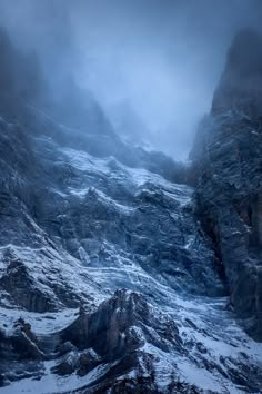 the mountains are covered in snow and ice as they rise up into the sky on a foggy day