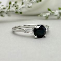 a white gold ring with an oval cut black diamond and baguettes on the side