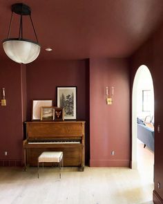 a living room filled with furniture and a piano in front of a red painted wall