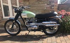 a green and white motorcycle parked in front of a brick building next to some flowers