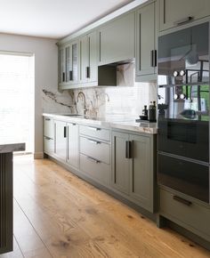 a large kitchen with wooden floors and gray cabinets, marble backsplash on the wall