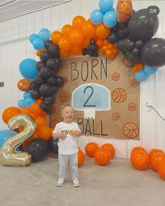 a young boy standing in front of a basketball themed wall with balloons and numbers on it