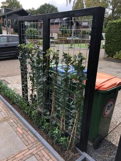 a fenced in area with plants growing out of it and a garbage can next to it