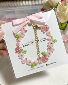 a hand holding a pink and green bracelet with flowers in the background on a card