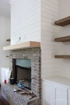 the fireplace is being built with white shiping on the walls and wood shelves around it