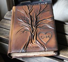 a brown leather book with a tree and heart on the cover, sitting on top of a wooden bench