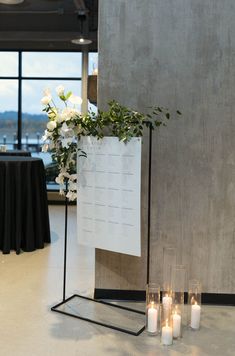 candles are lit in front of a sign with flowers and greenery next to it