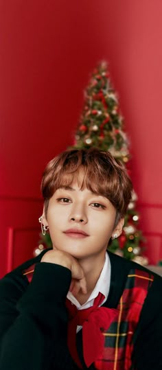 a young man sitting in front of a christmas tree with his chin resting on his hand