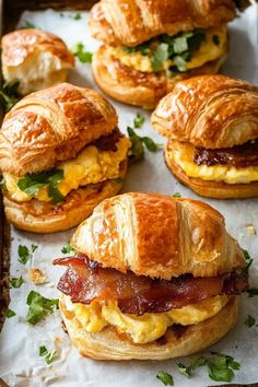 breakfast sandwiches and croissants with bacon on them sitting on wax paper lined up