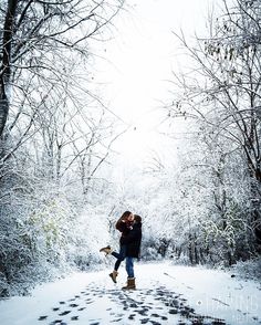 a man and woman are walking through the woods in winter with footprints on the ground