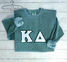 a green sweatshirt with the letters ka on it and a bow at the front, sitting on a white wooden floor