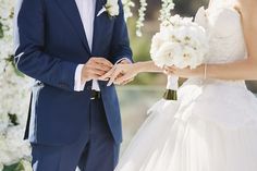 the bride and groom are holding hands under an arch of white flowers at their wedding ceremony