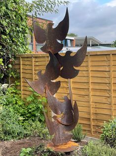 a tall metal sculpture sitting in the middle of a garden next to a wooden fence