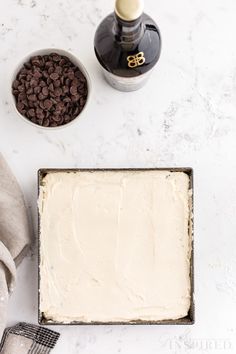 a cake with white frosting and chocolate chips next to a bottle of wine on a table