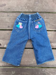 a pair of blue jeans with pink flamingos embroidered on the front and back, sitting on a wooden surface