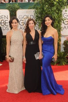 three women in dresses standing on a red carpet